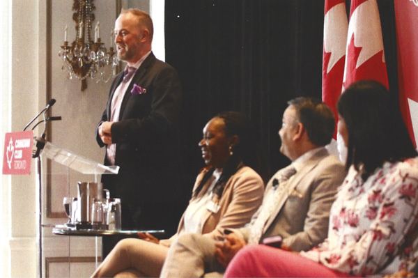 Michael Bach addressing the Canadian Club of Toronto from the podium with a panel seated behind him.